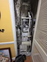 Commercial AC Heating Repair in Atlanta Dunwoody 30338 by The Air Company of GA.  Opened furnace unit in a closet with exposed pipes, ducts wrapped in foil insulation, and a tool bag on wooden floor.