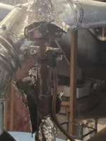 Residential AC Cooling Repairs in Sandy Springs 30350 by The Air Company of GA. Close-up of old metal pipes and valves wrapped with torn foil insulation in a basement storage area.