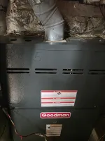 Goodman furnace unit with warning labels and connected duct pipe in a basement setting.  Commercial Goodman HVAC Repair in Marietta 30060 by The Air Company of GA