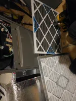 Two HVAC air filters next to an open furnace with tools on a wooden floor during maintenance.