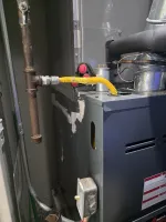 Commercial HVAC Repair in Dunwoody 30338 by The Air Company of GA.  Close-up of a gas furnace with yellow flexible gas line connected to metal pipe inside a utility room.