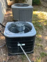 Residential AC Maintenance in Norcross by The Air Company of GA. Technician using gauge manifold to check air conditioner unit pressure outdoors on grassy ground near red bucket.