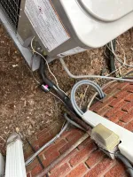 AC Cooling Dehumidification System Installation in Atlanta 30307 by The Air Company of GA. Outdoor HVAC unit with connected insulated pipes and electrical conduit mounted on red brick wall and soil ground.