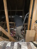 Commercial HVAC Repair in Atlanta 30324 by The Air Company of GA.  Worker wearing a hoodie and pants inspecting ductwork in a wooden attic space with insulation and pipes.