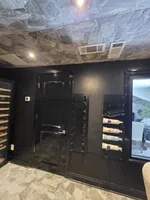 Wine Cellar Installation in Atlanta by The Air Company of GA.  Black wall with mounted wine racks holding bottles next to a closed black door and stone ceiling and floor.