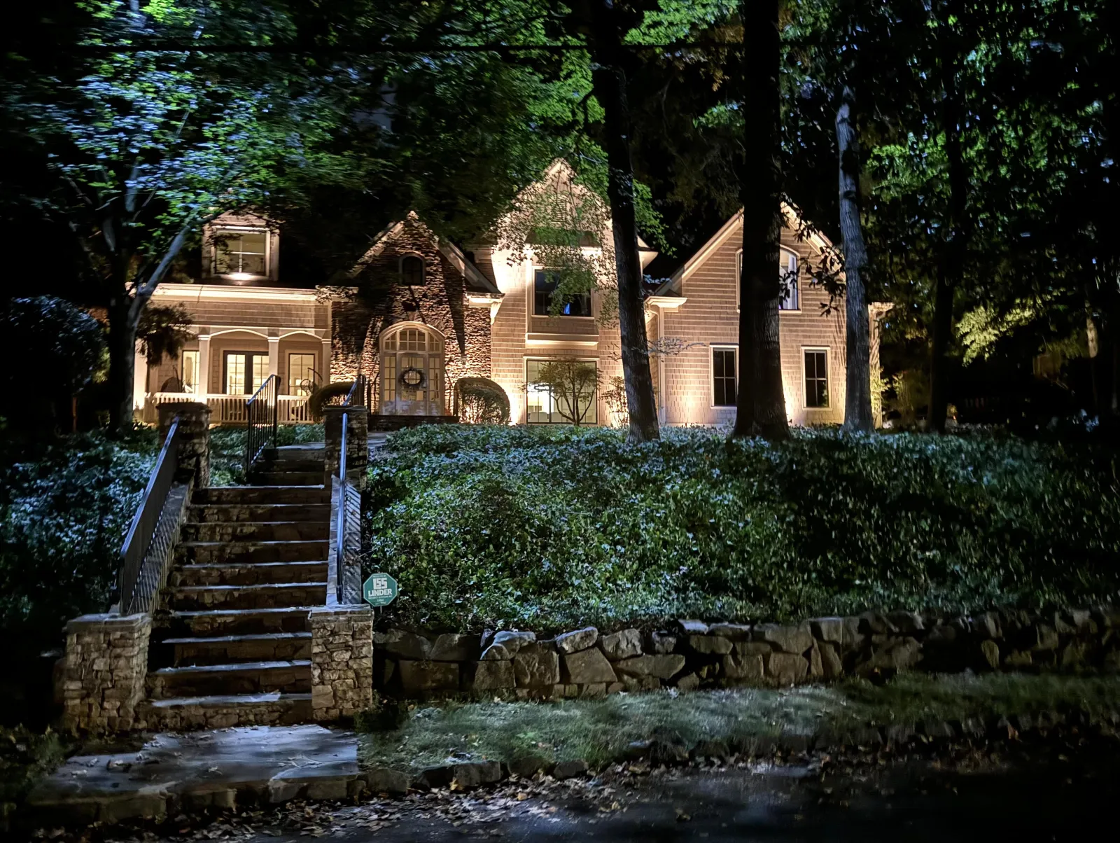 Elegant Atlanta home illuminated with professional landscape lighting highlighting architectural features, stone staircase, and mature trees, creating a warm and inviting nighttime curb appeal by Gibbs Landscape Company.