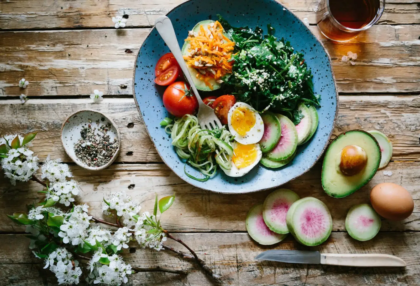 A table with food on a plate, a drink in a cup, and a variety of food items and flowers strewn across the table