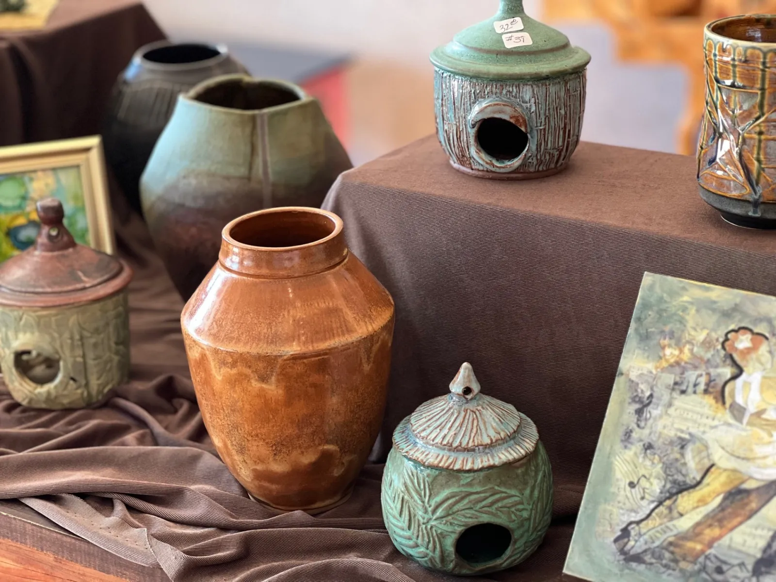 Assorted handcrafted ceramic pots and decorative jars displayed on brown fabric at an art market.