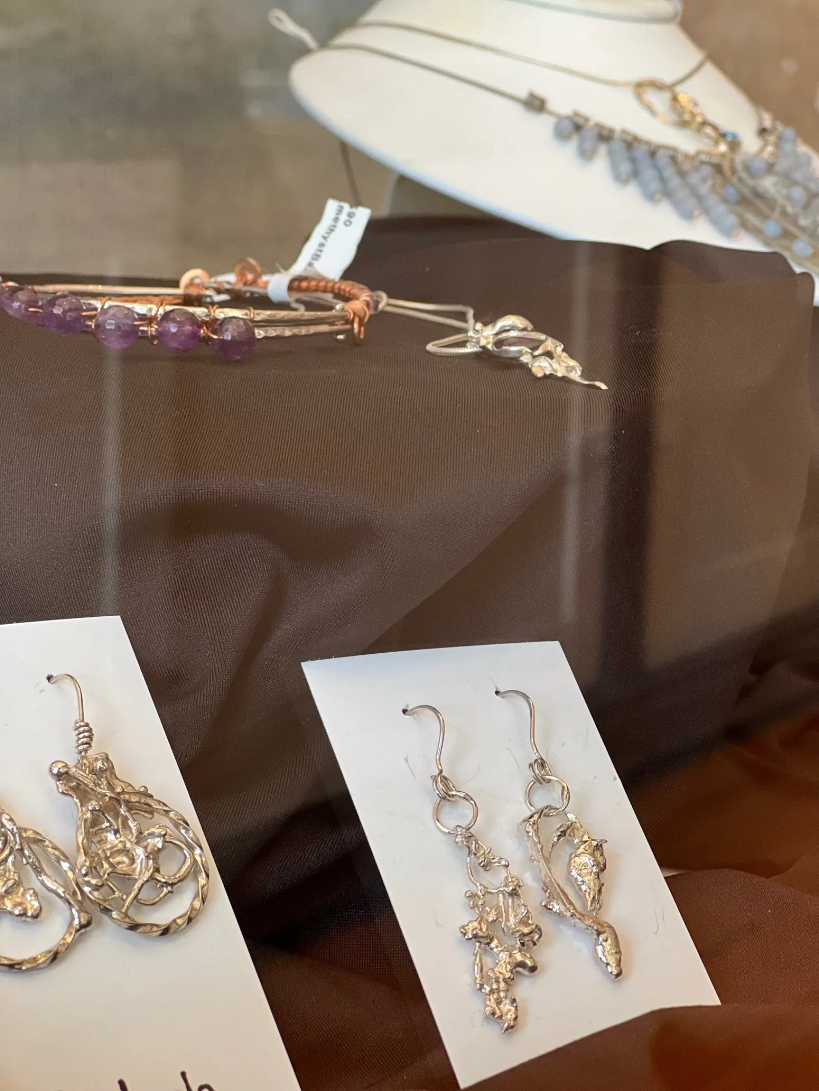 Display of handcrafted silver earrings and beaded bracelets on brown fabric in a jewelry showcase.