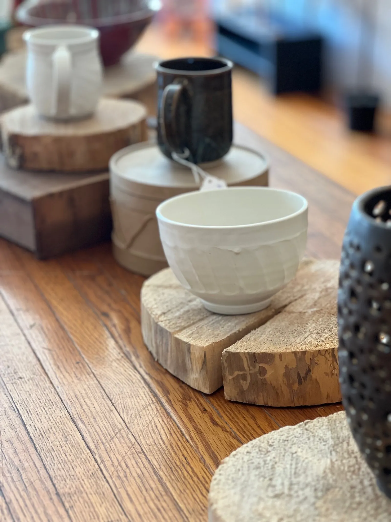 White and black ceramic cups on rustic wooden coasters arranged on a wooden table with natural light.