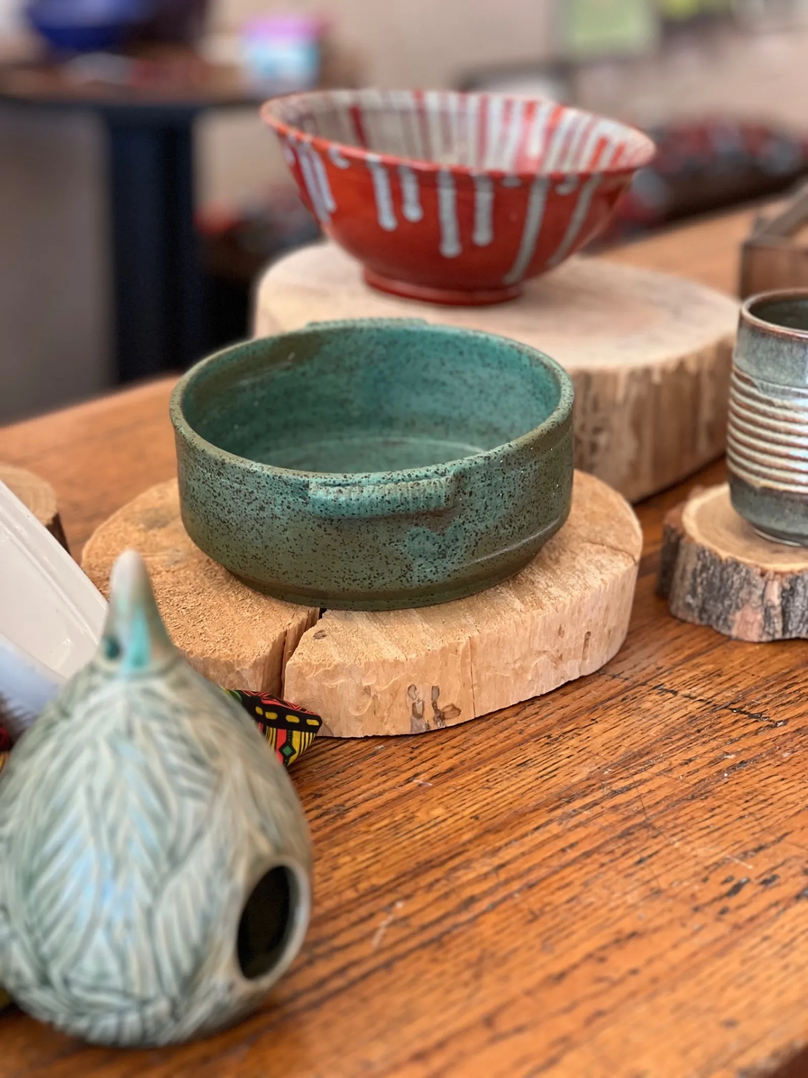 Various handcrafted ceramic bowls and vessels displayed on wooden slices on a rustic wooden table.
