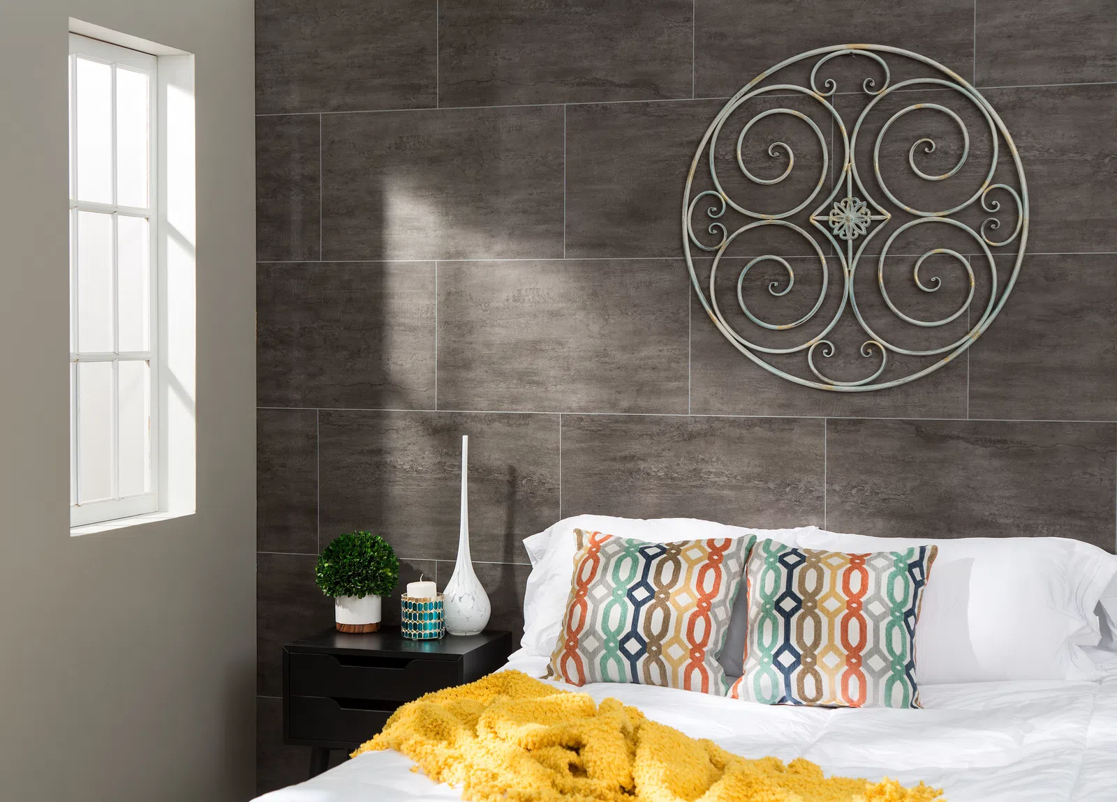 Cozy bedroom with patterned pillows, yellow throw blanket, decorative wall art, and natural light from window