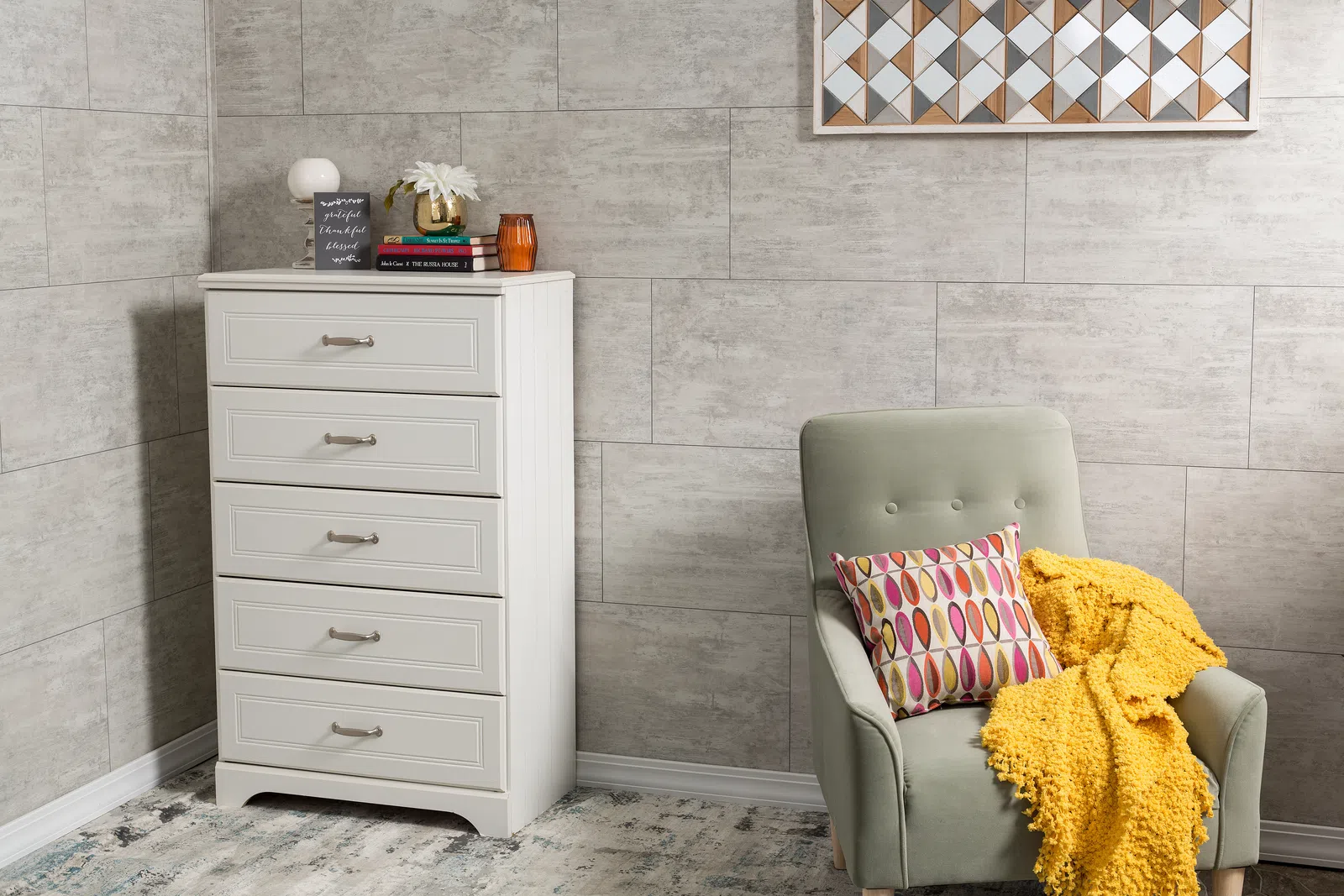 Cozy corner with light gray tall dresser beside green armchair with multicolored pillow and yellow throw blanket
