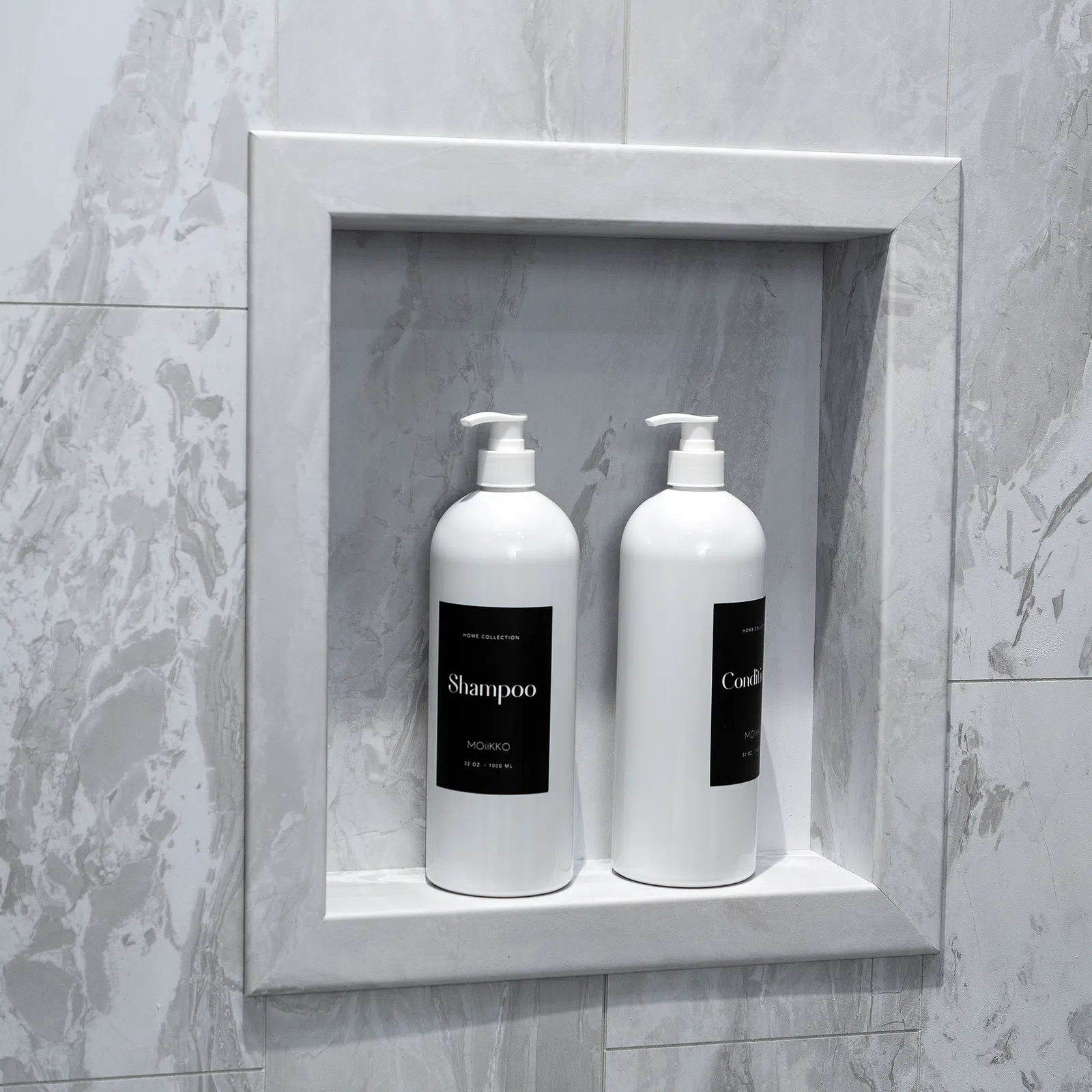 Two white pump bottles of shampoo and conditioner in a recessed marble shower niche.