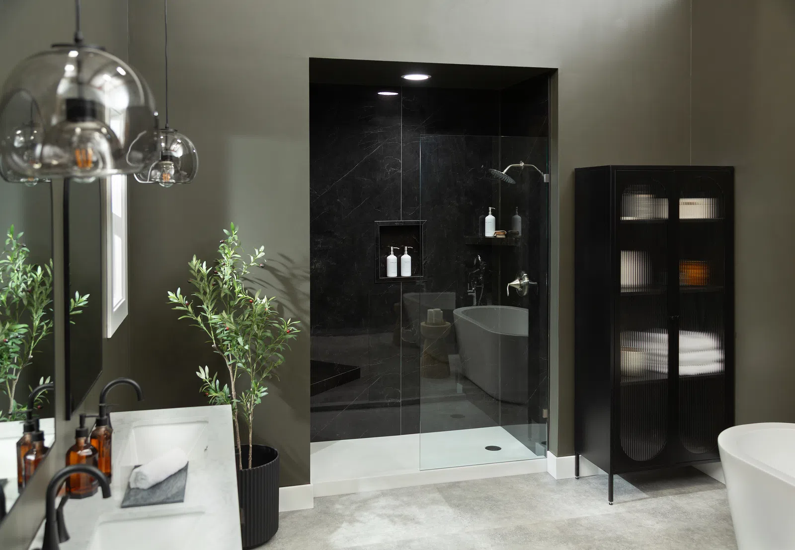 Modern bathroom with glass shower, black cabinet, freestanding tub, and green plant accents in neutral tones