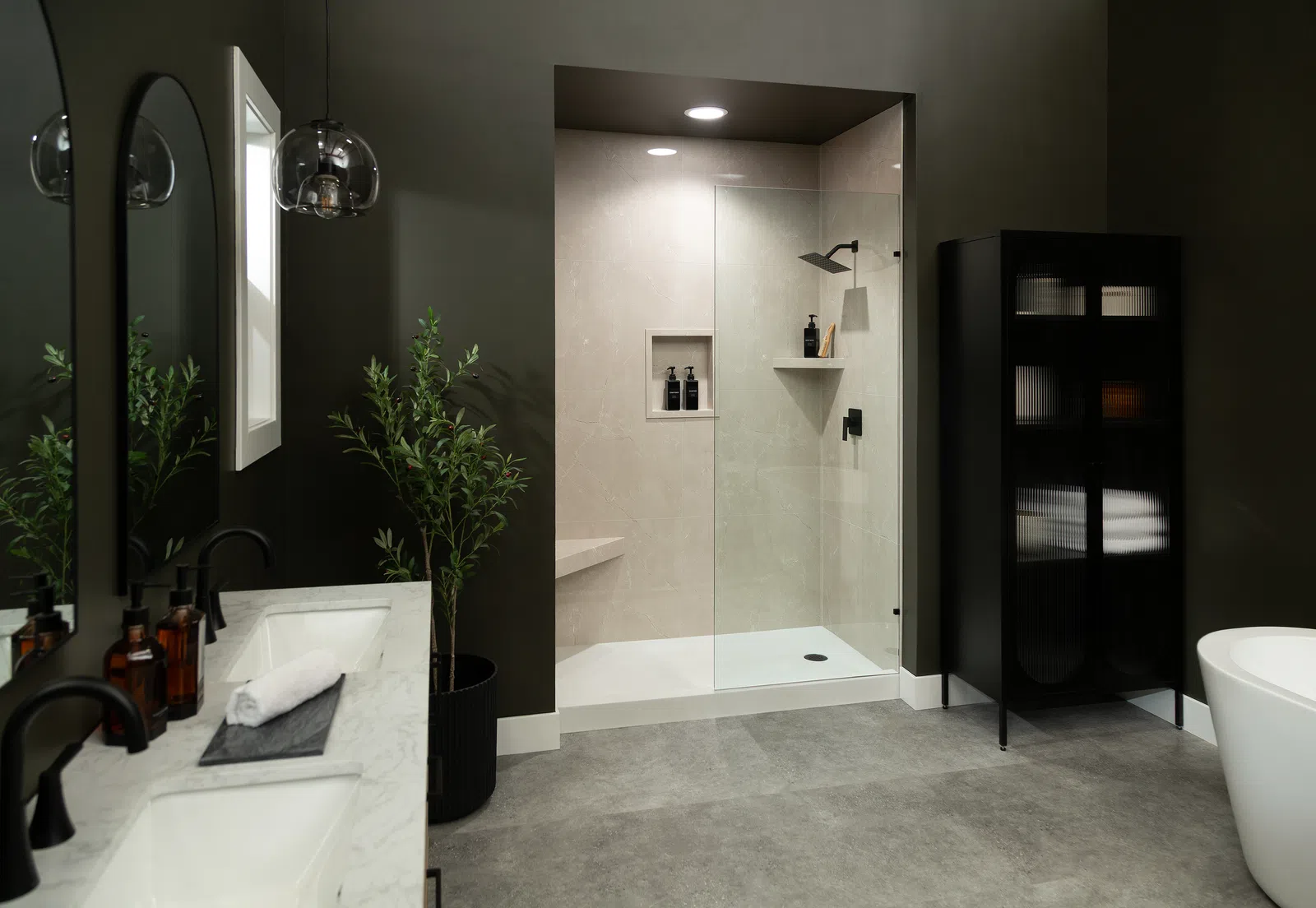 Modern bathroom with glass shower enclosure, black fixtures, marble countertop, and dark cabinetry with plants.