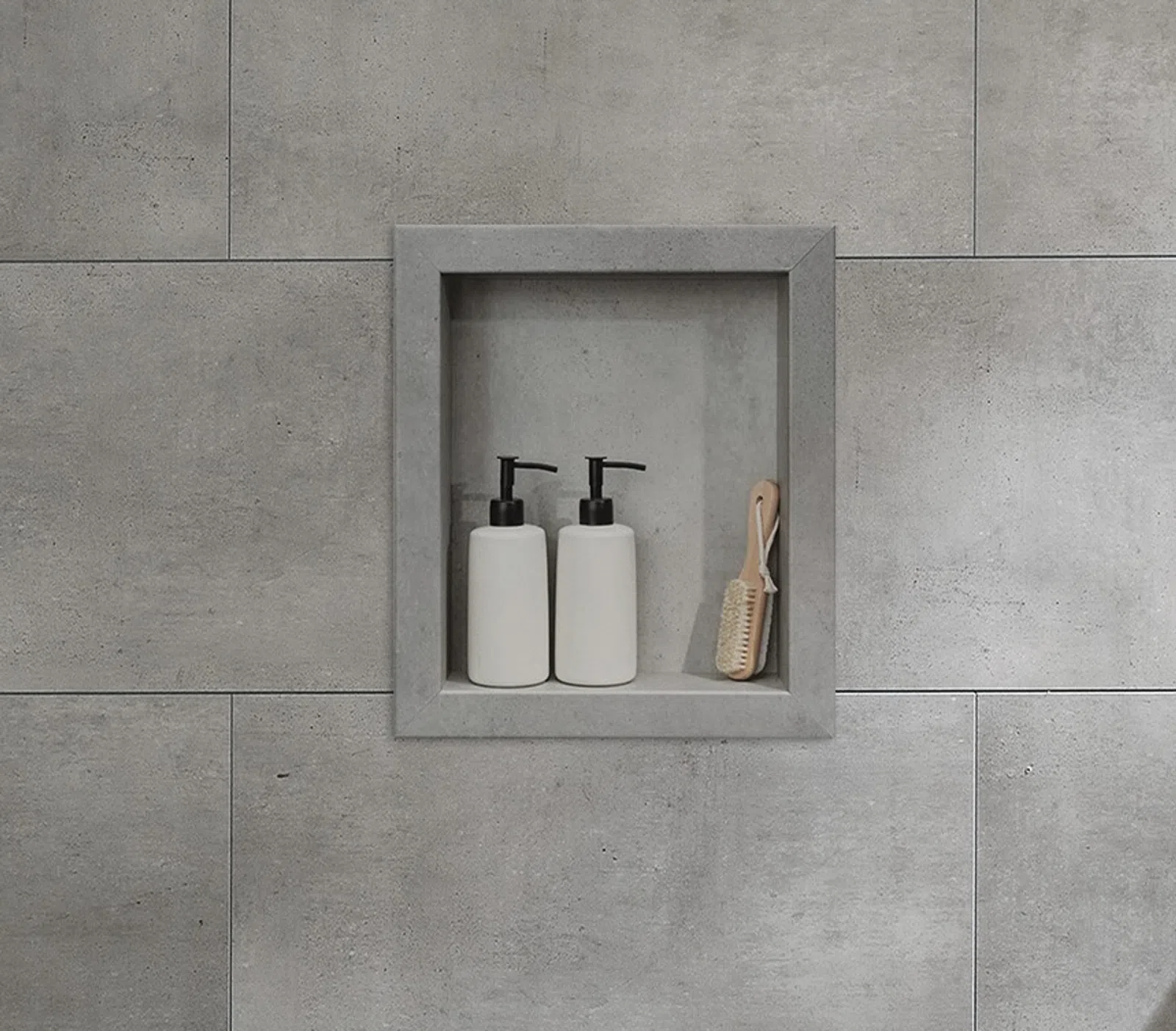 Built-in gray tiled shower niche holding two white pump bottles and a small wooden brush.