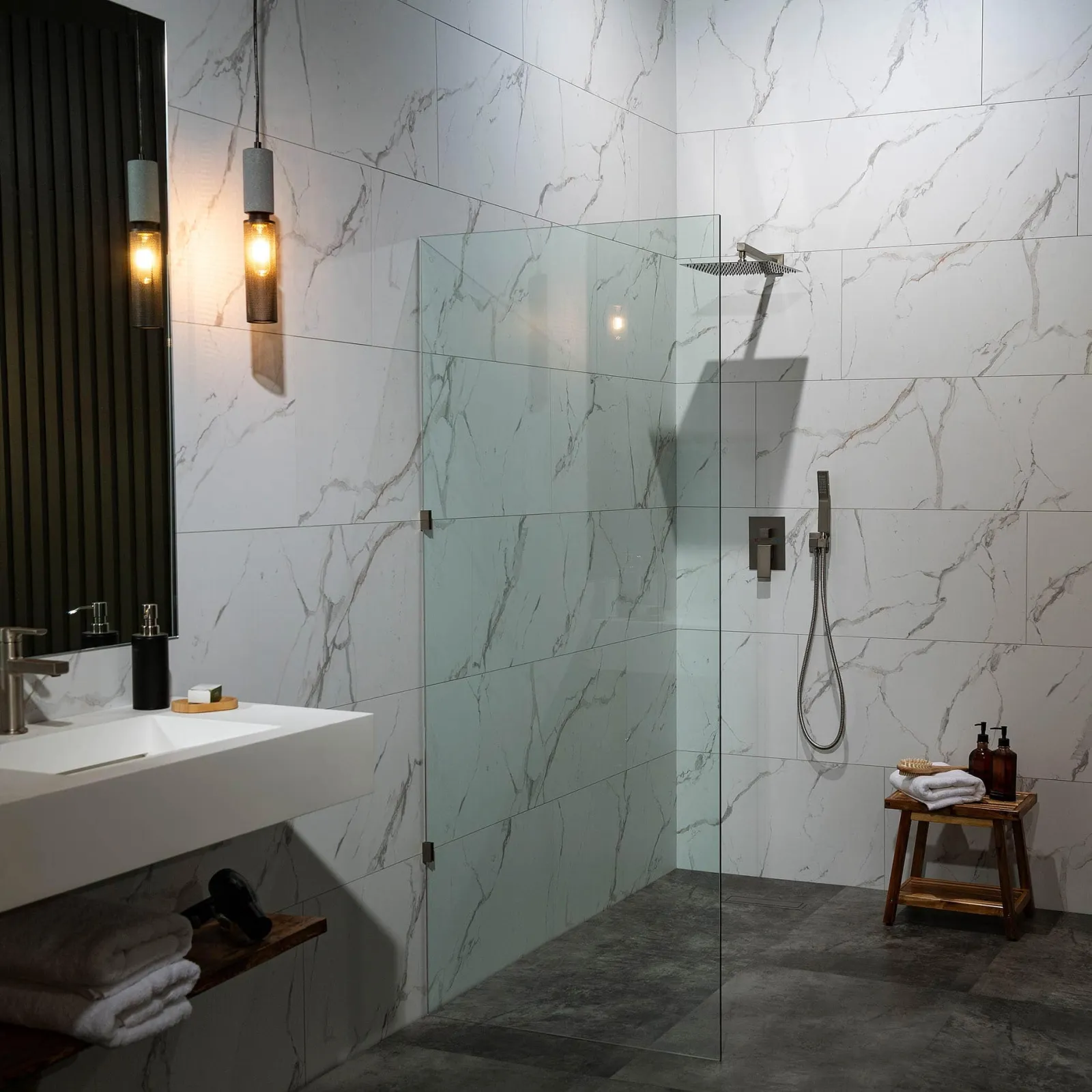 Modern bathroom with marble tiles, glass shower partition, wooden stool, and pendant lighting
