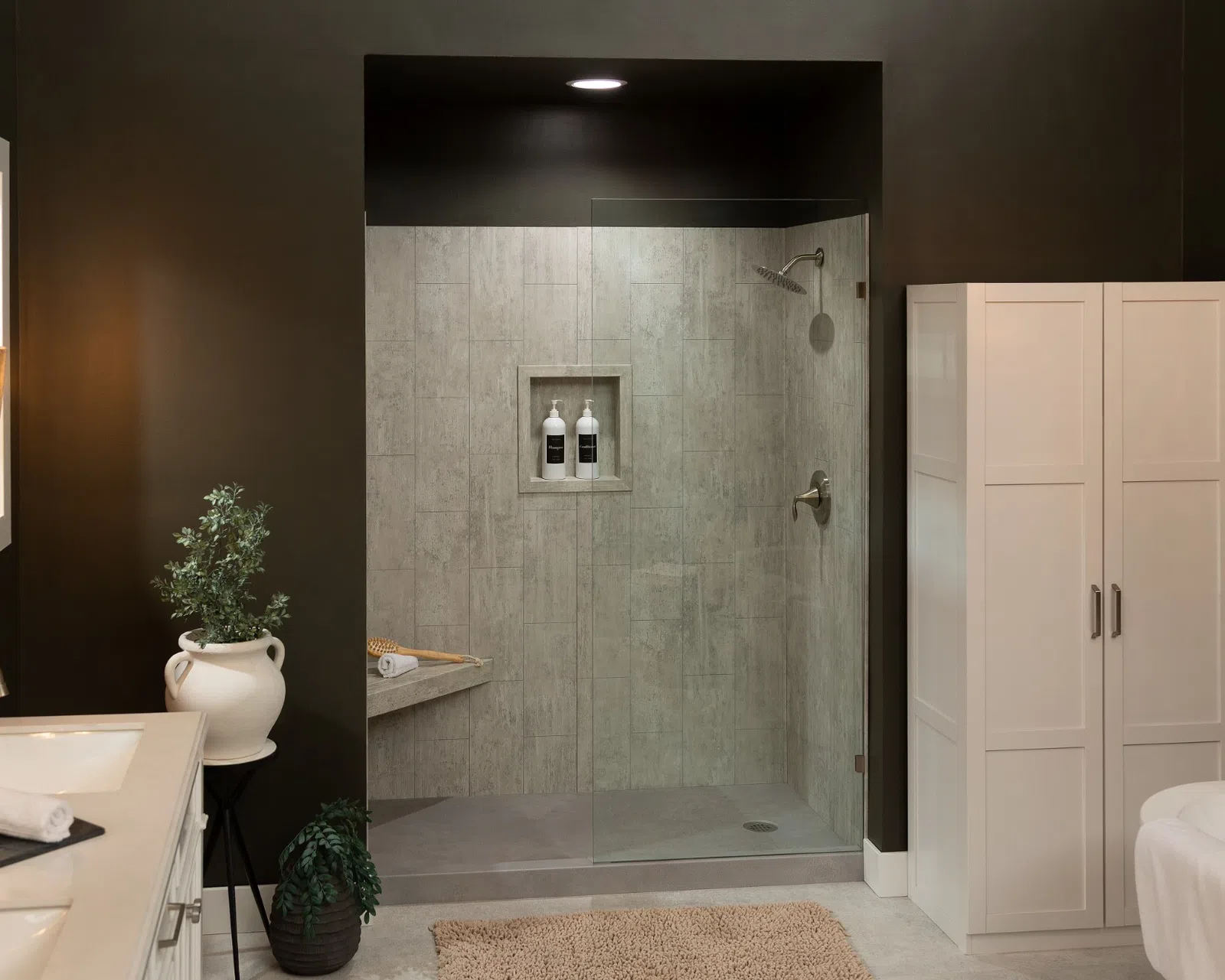 Modern bathroom with double sink, glass shower enclosure, dark walls, and white storage cabinet with plants.
