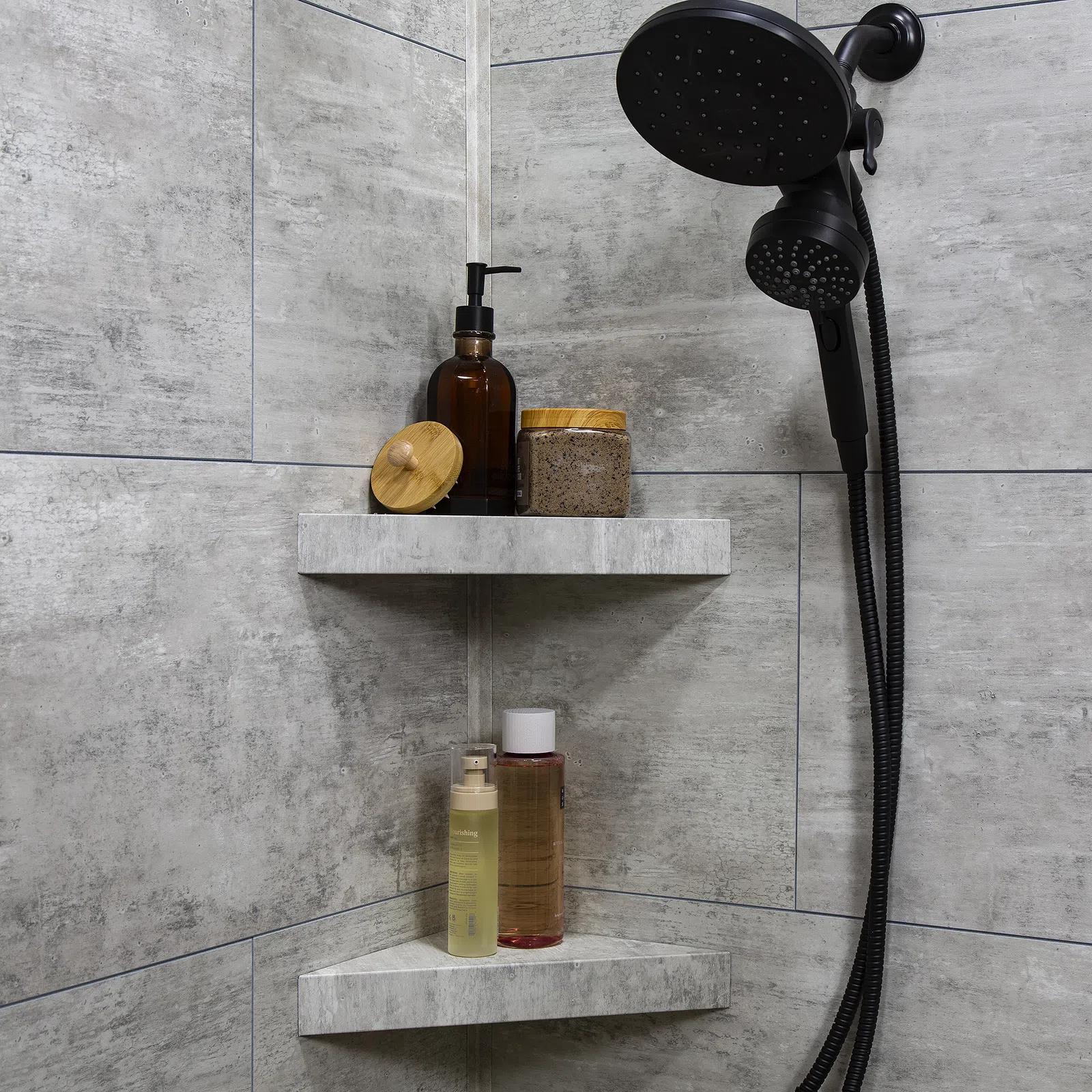 Modern shower corner with black showerhead and shelves holding toiletries in a gray tiled bathroom.