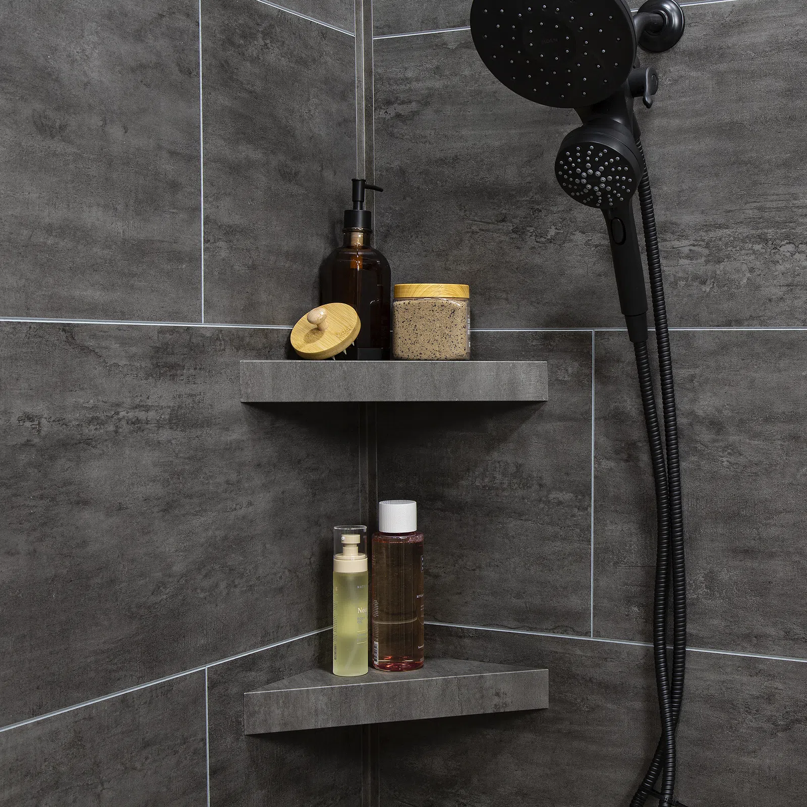 Modern corner shower shelves with bottles and jars against dark gray tiled bathroom walls.