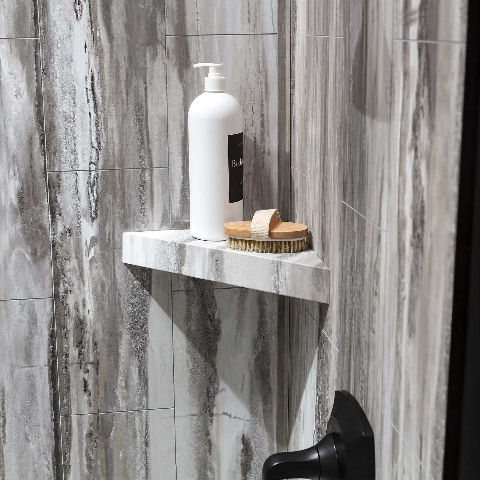 White pump bottle and wooden brush on marble corner shelf in gray tiled shower area