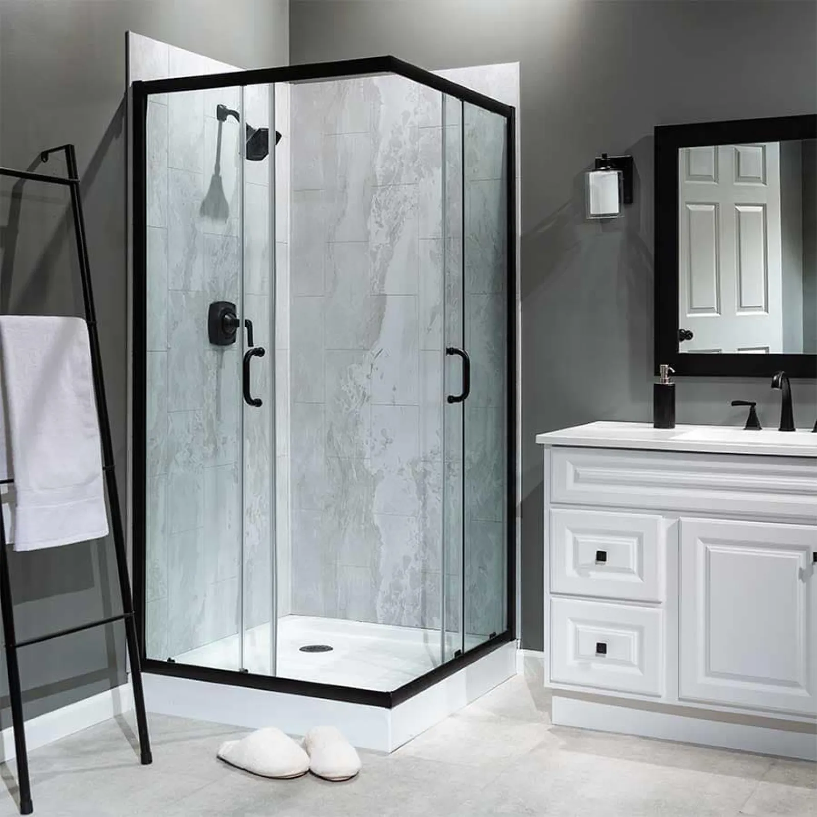 Modern corner glass shower with black frame, gray tile walls, white vanity, and towel rack in sleek bathroom