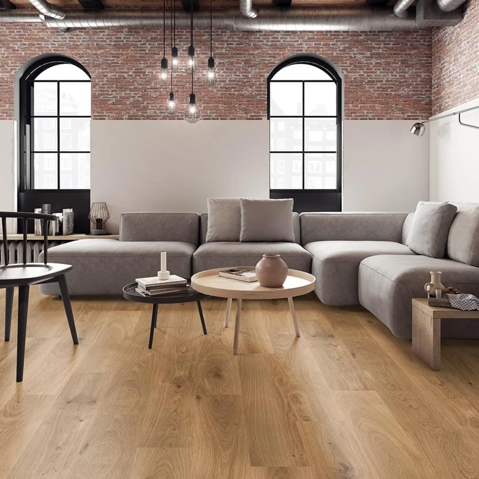 Modern living room with gray sectional sofa, wooden coffee tables, exposed brick wall, and large arched windows.