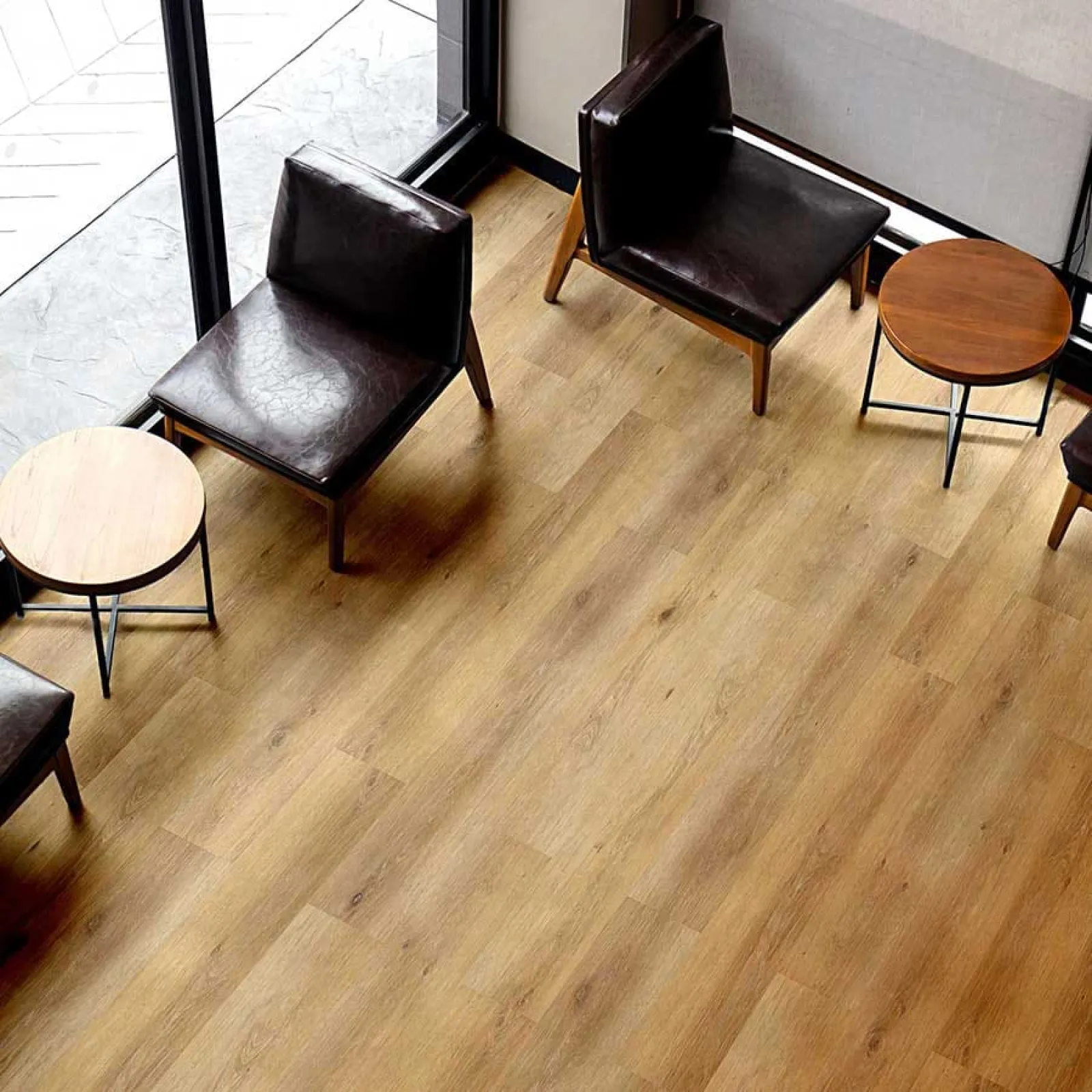 Modern seating area with dark leather chairs and round wooden tables on light hardwood floor near large windows.