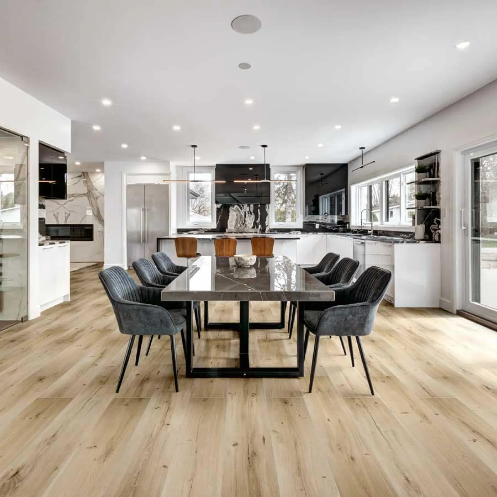 Spacious modern kitchen and dining area with black marble table, gray chairs, wood flooring, and large windows.