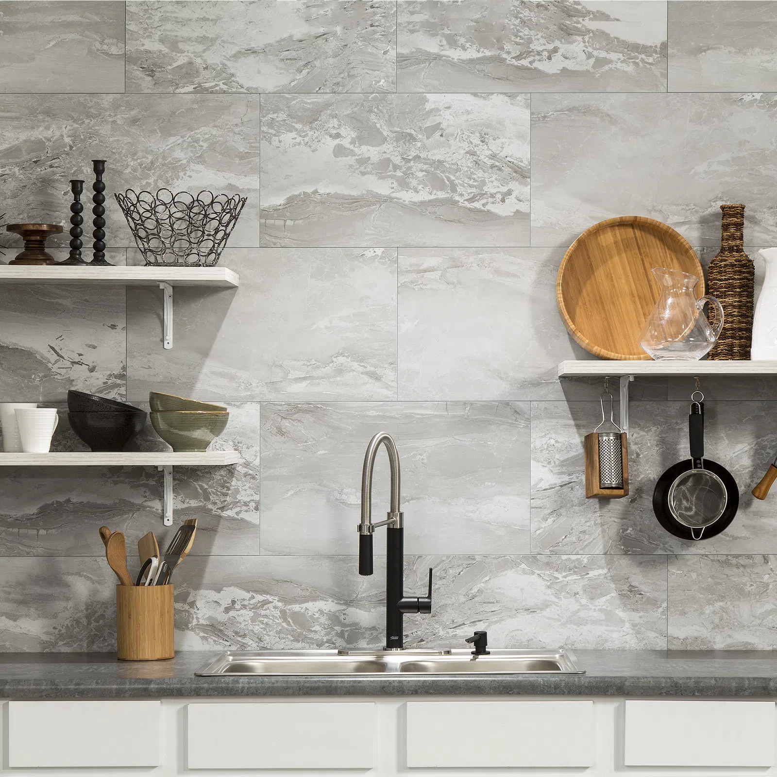 Modern kitchen sink with black faucet, marble tile backsplash, floating shelves holding kitchenware and utensils.