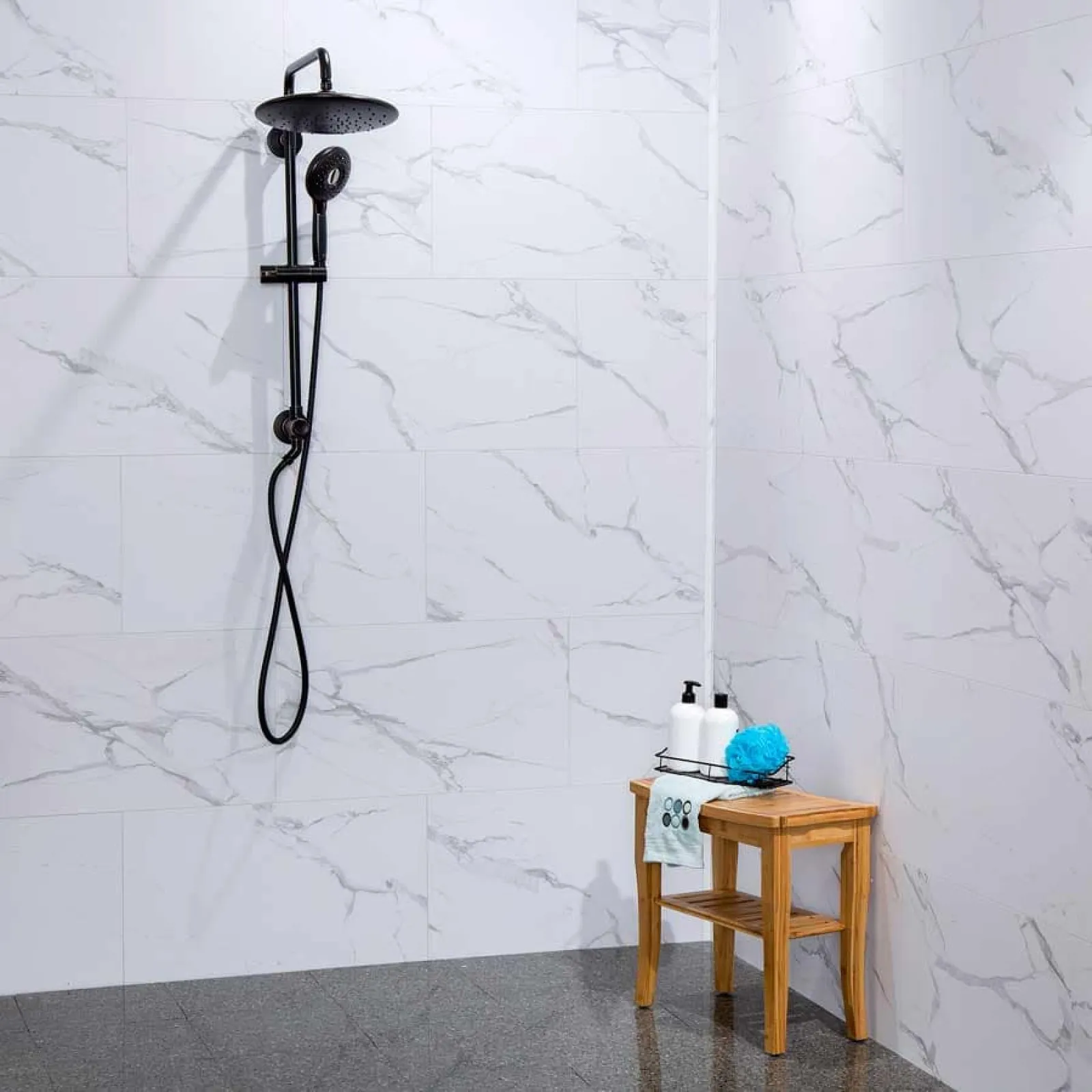 Modern shower with black fixtures and marble wall tiles next to a wooden stool with toiletries and a blue sponge.