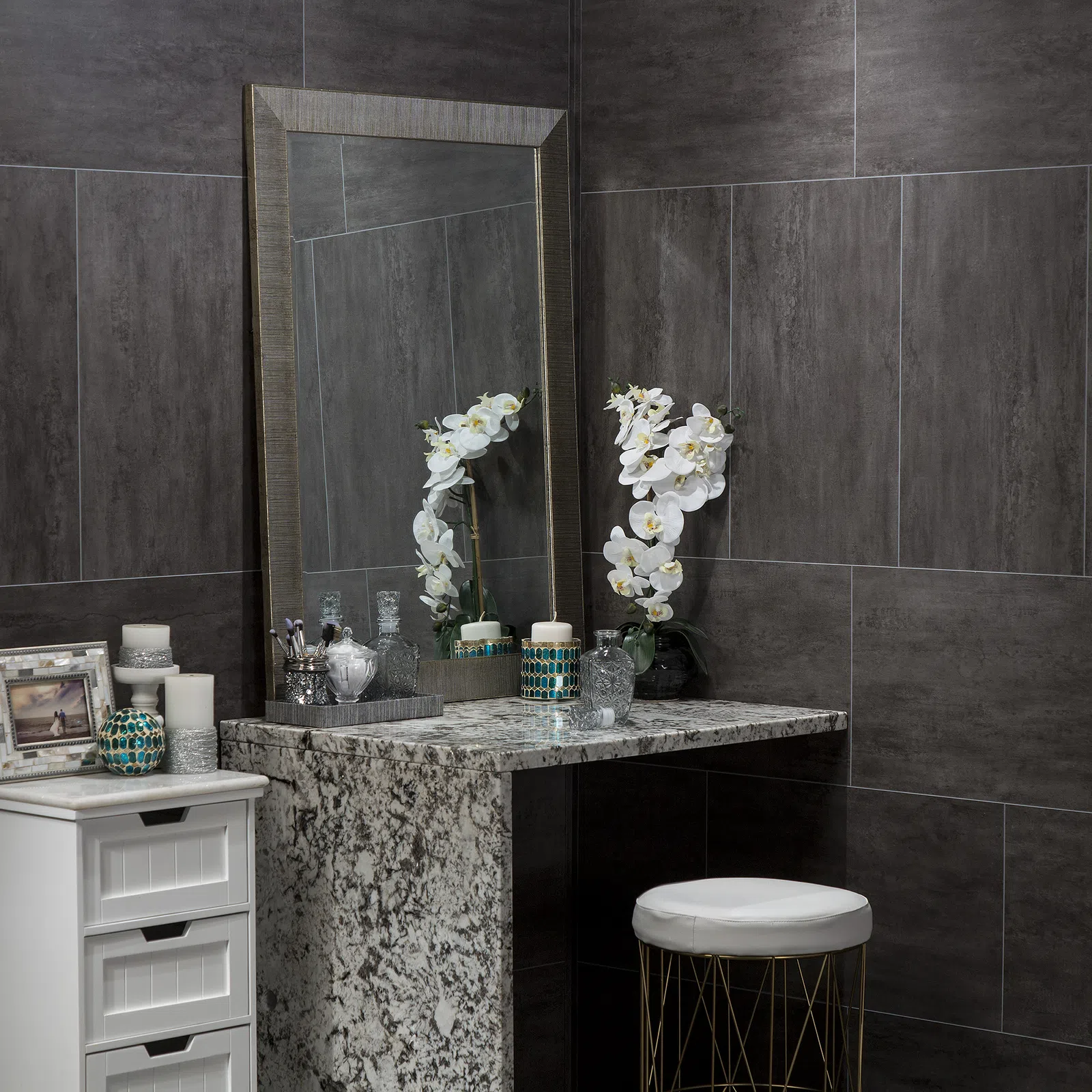 Modern vanity area with granite countertop, large mirror, white orchid, candles, and decorative items in gray tiled room
