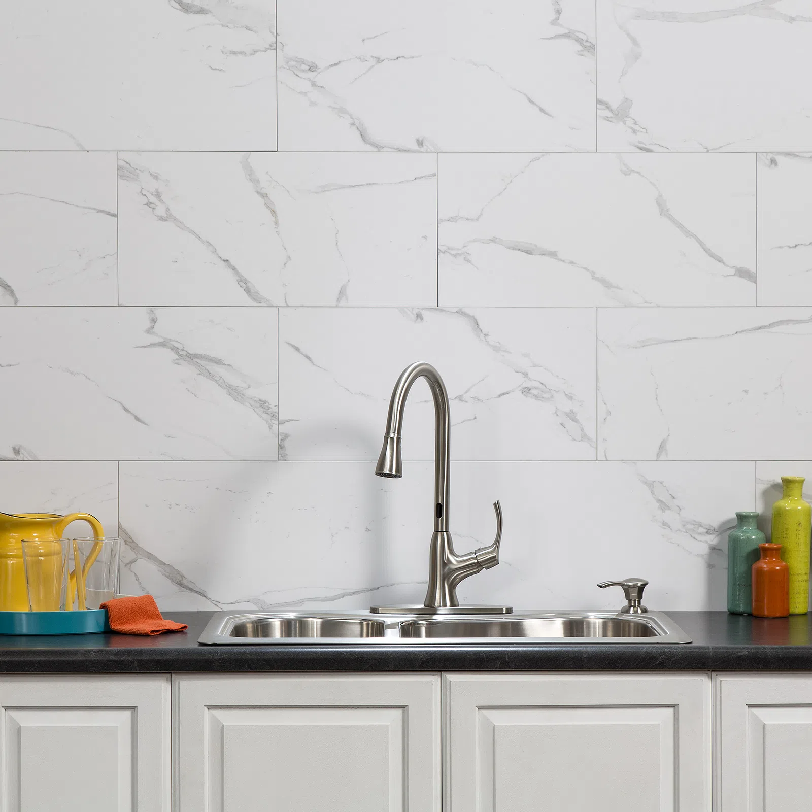 Modern kitchen sink with stainless steel faucet, black countertop, white marble backsplash, and colorful jars.
