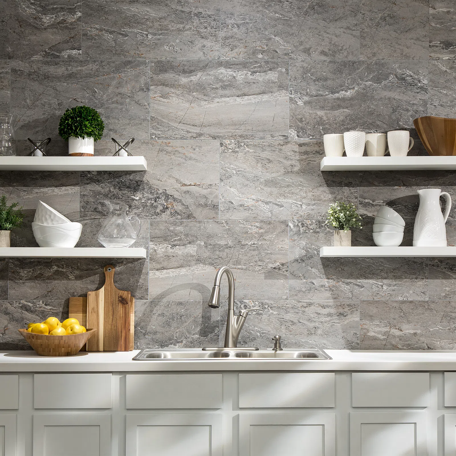 Modern kitchen sink with stainless faucet, white shelves, gray stone backsplash, and decorative kitchenware.