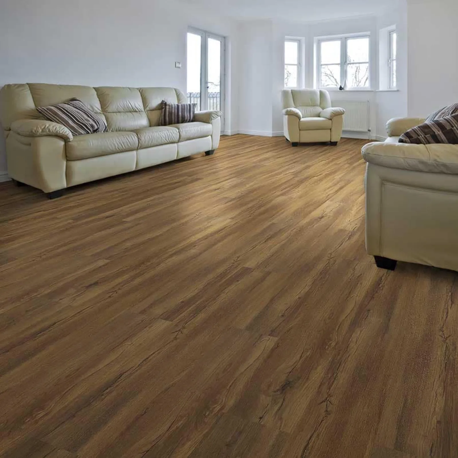 Bright living room with beige leather sofas and armchair on natural wood flooring with white walls and large windows