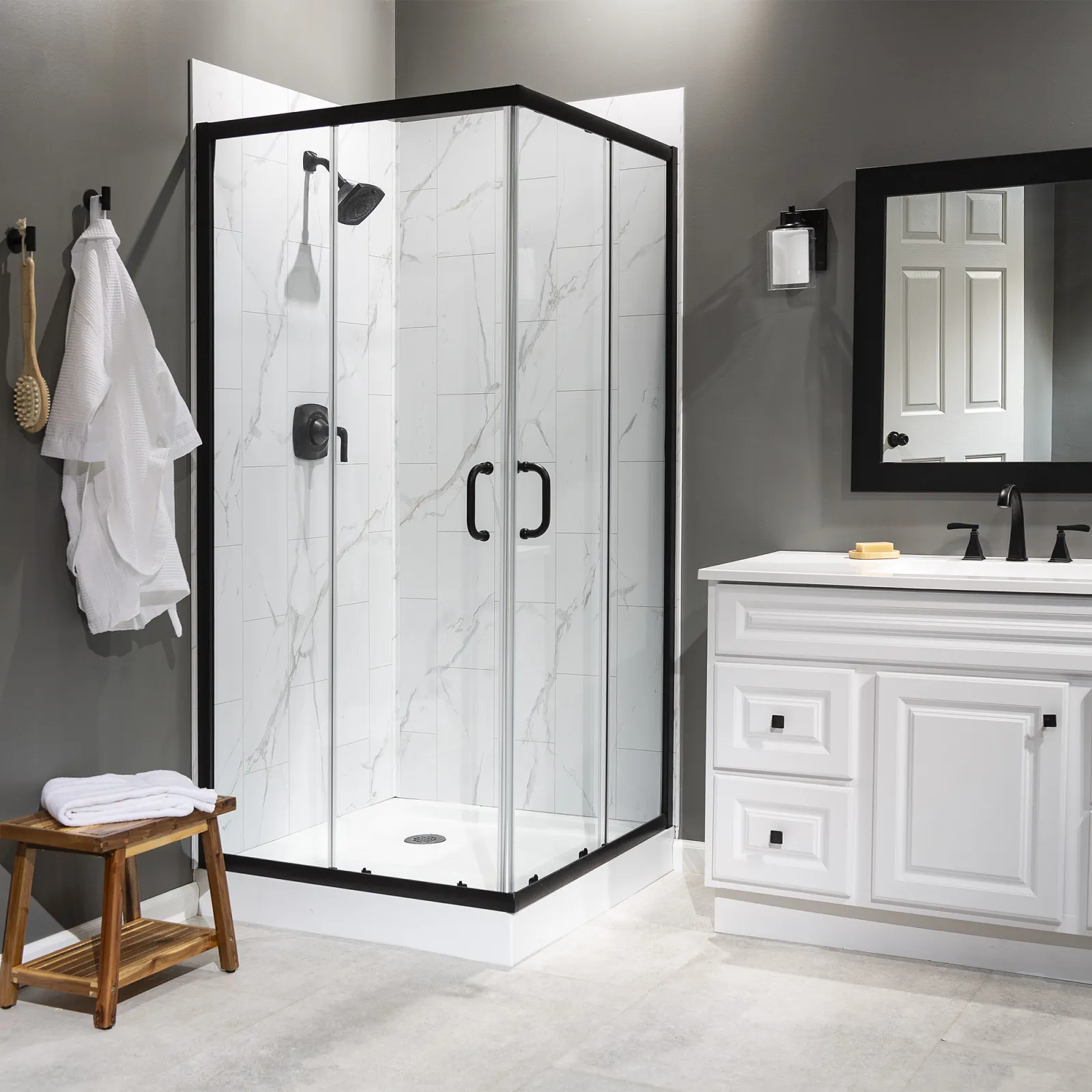 Modern bathroom with glass shower enclosure, white marble tiles, black fixtures, and white vanity with mirror.