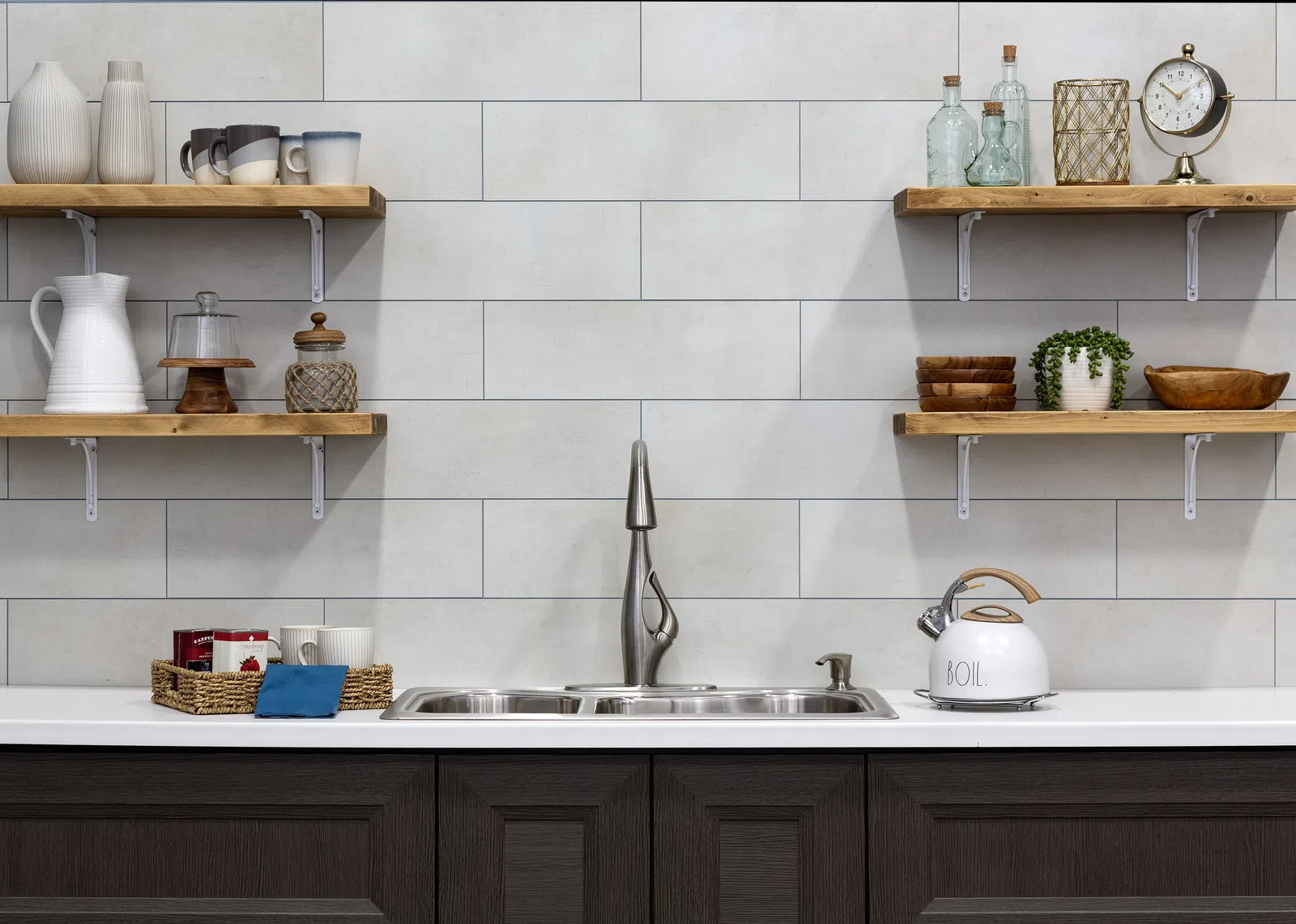 Modern kitchen sink with dark cabinets, floating wooden shelves holding glassware, mugs, and decorative items.