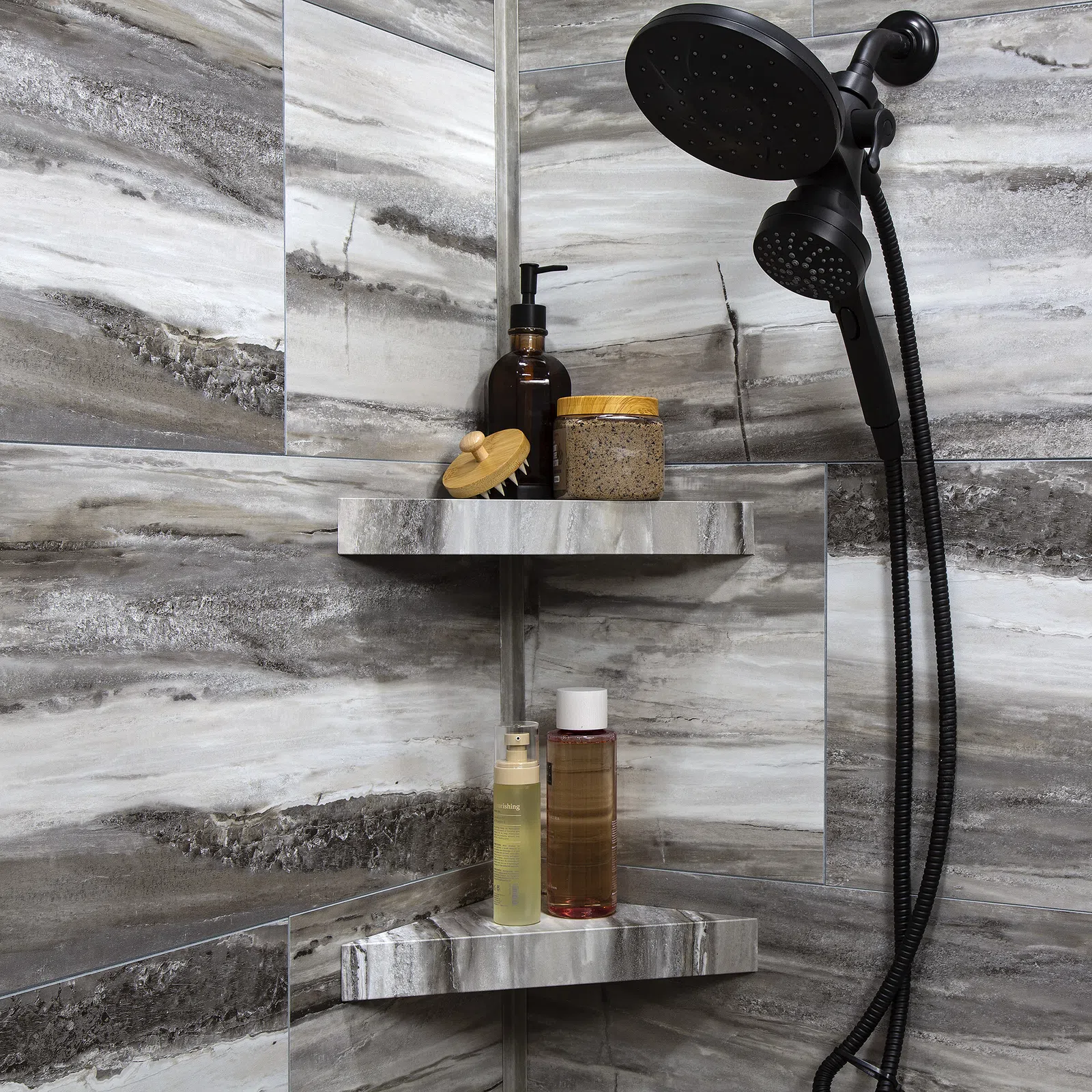 Modern shower corner with gray marble tiles, black showerhead, and shelves holding bath products and brush.