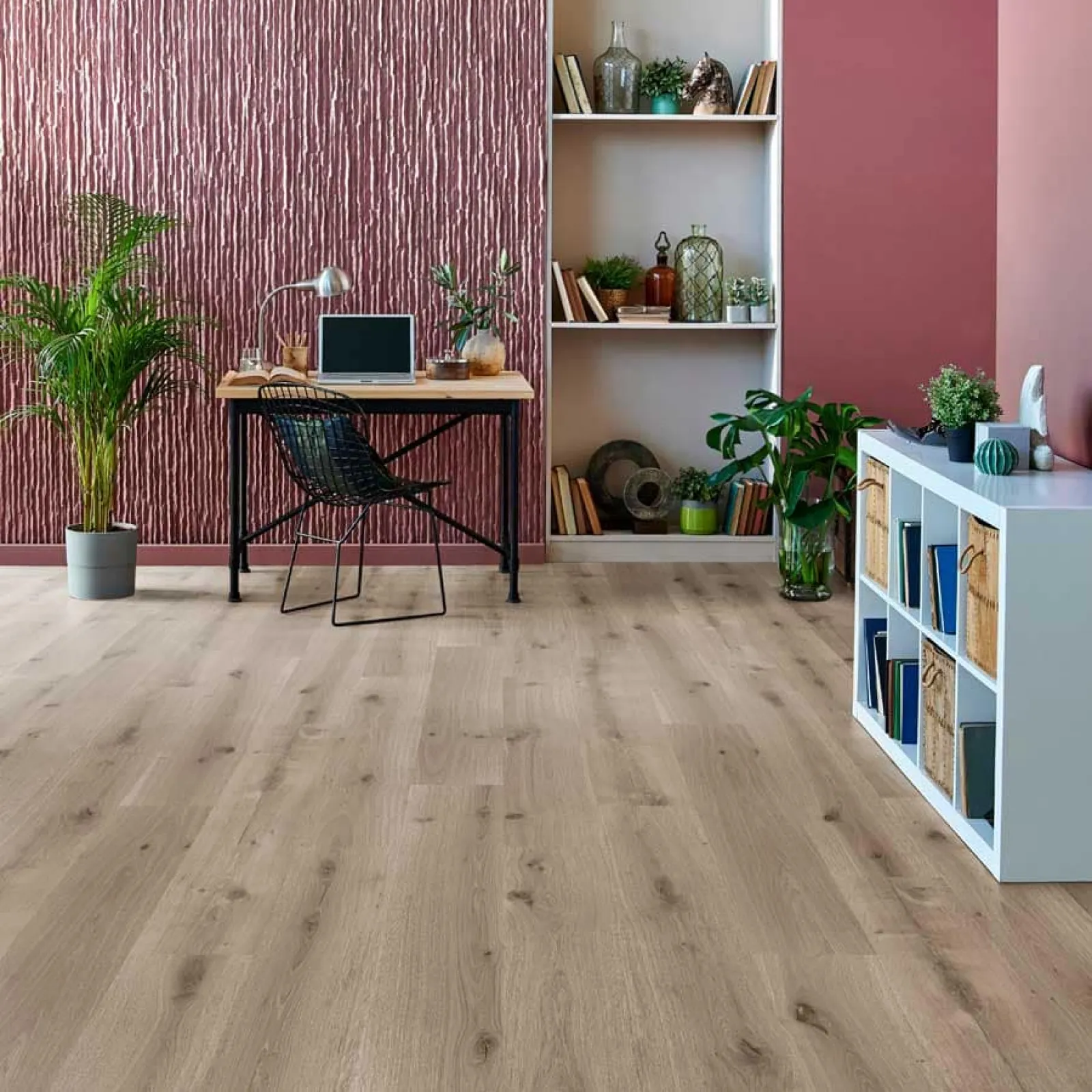 Modern home office with light wood flooring, textured mauve accent wall, plants, and minimalist furniture setup
