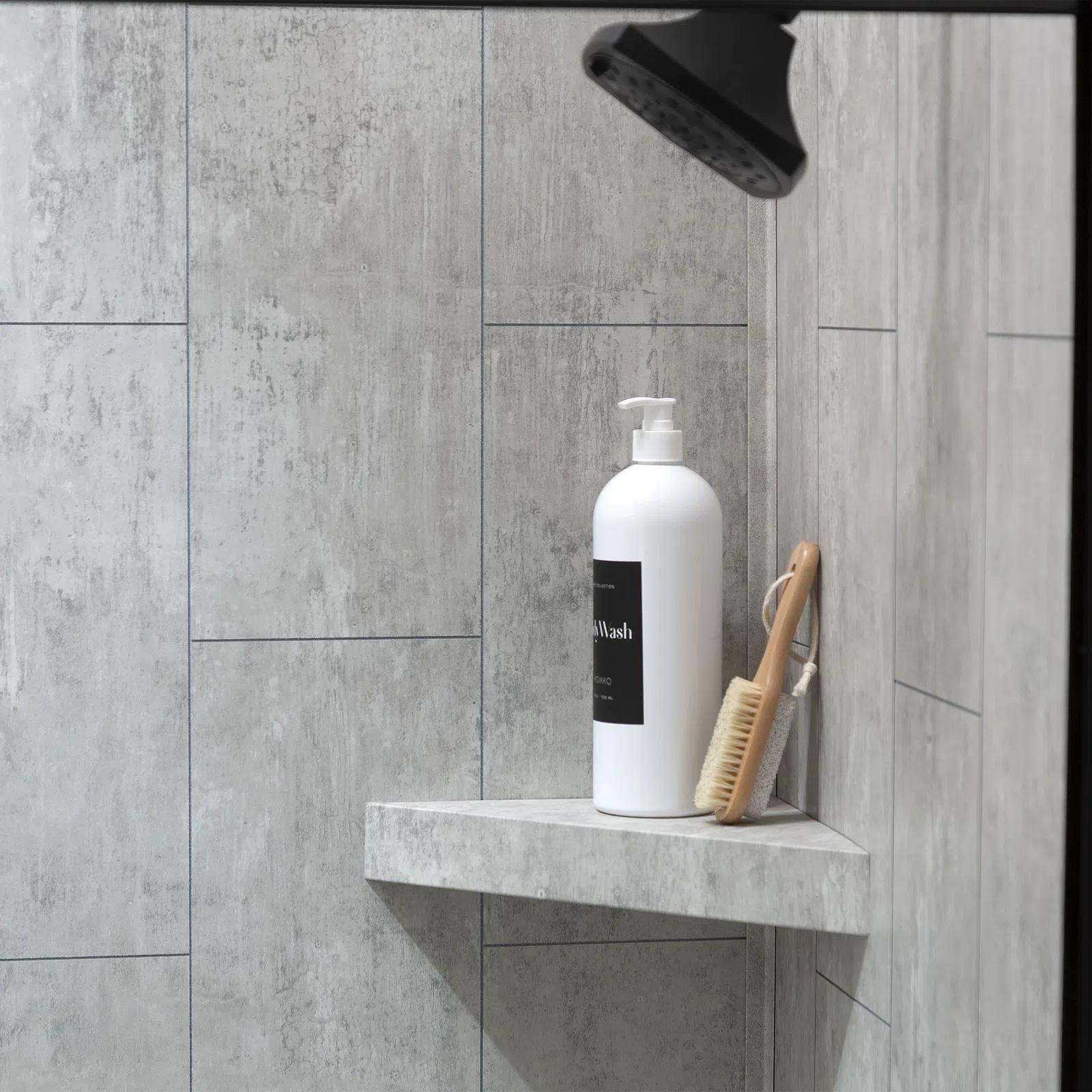 White pump bottle and wooden brush on corner shelf in modern gray tiled shower area under black showerhead.