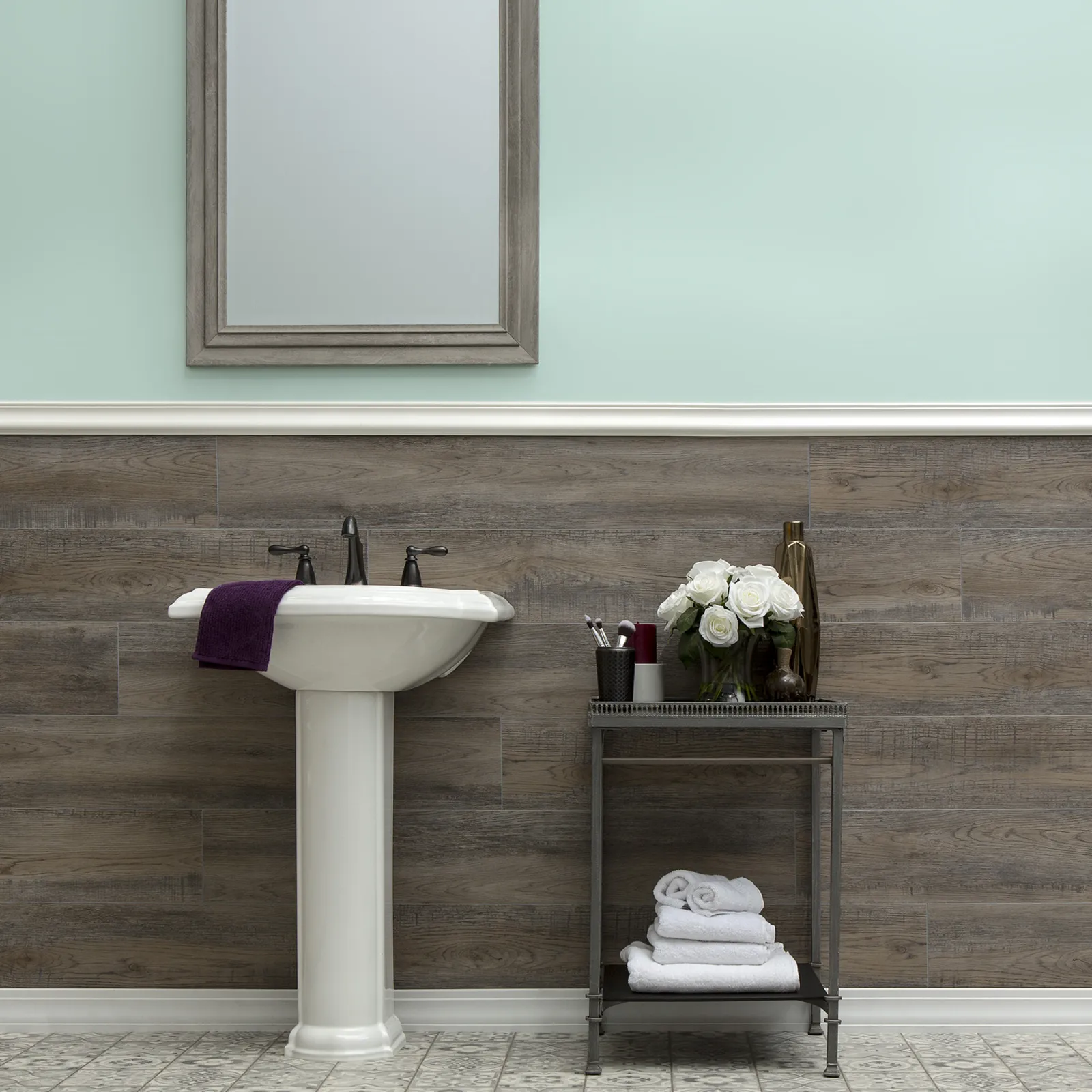 Modern bathroom with pedestal sink, wooden panel wall, light mint paint, mirror, and decorative towels and flowers.