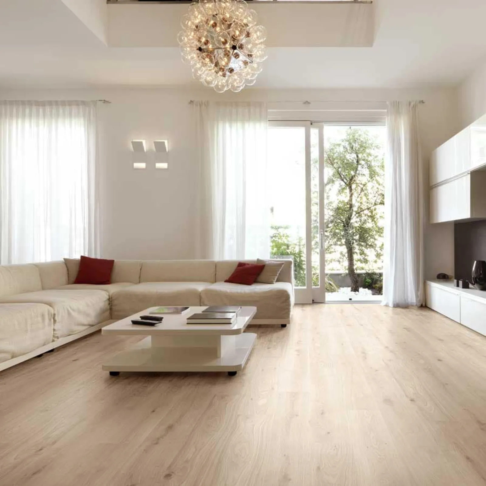 Modern living room with beige sectional sofa, wooden floor, white coffee table, large windows, and chandelier lighting