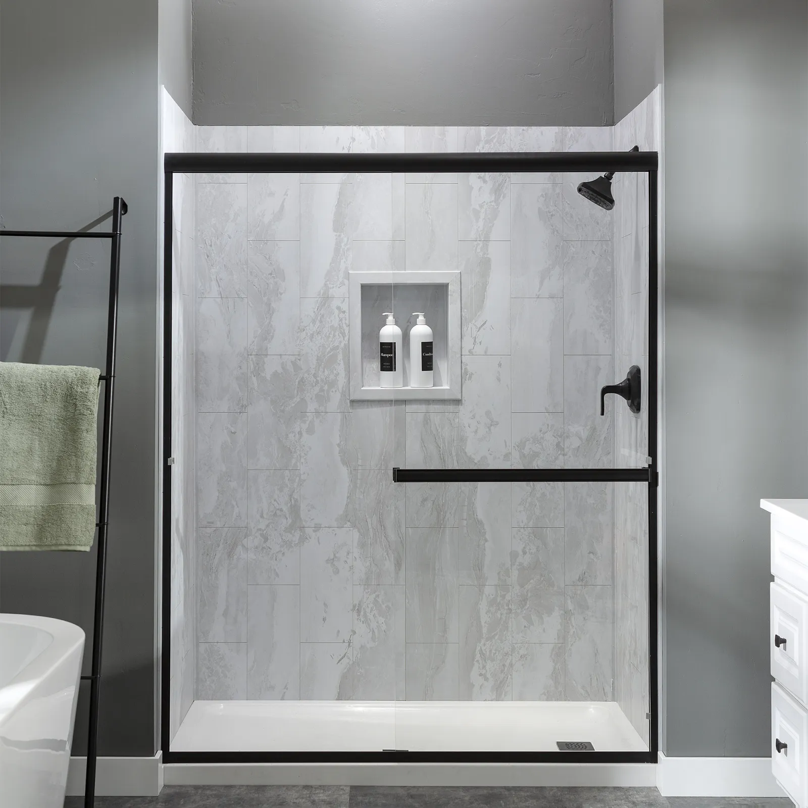 Modern bathroom shower with glass door, black fixtures, marble tiles, and built-in shelf with bottles.