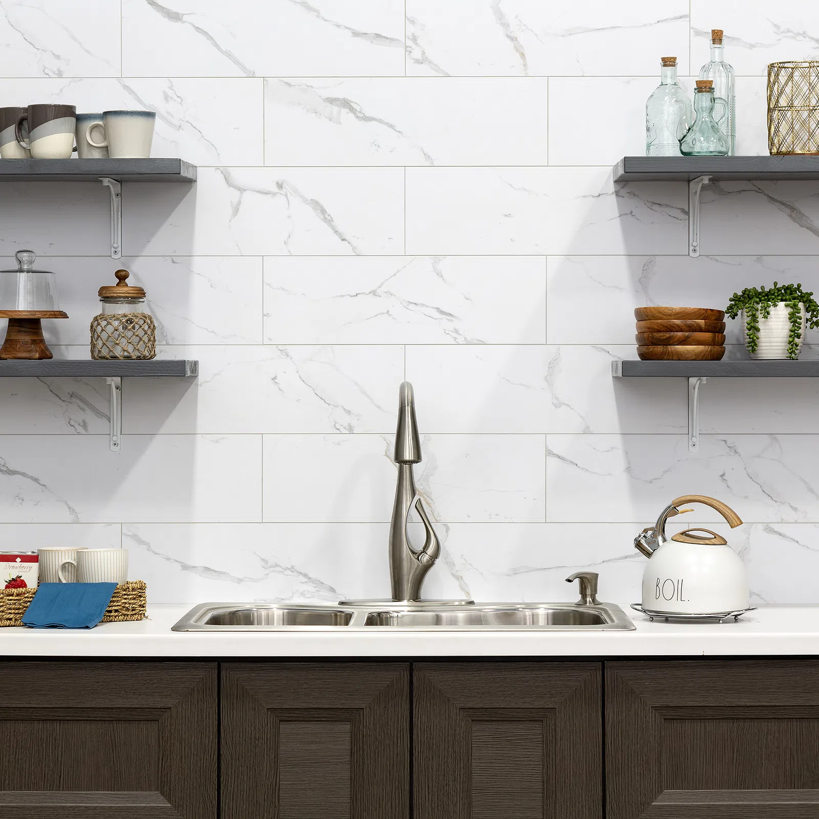 Modern kitchen with stainless steel sink, sleek faucet, marble backsplash, floating shelves, and white kettle.
