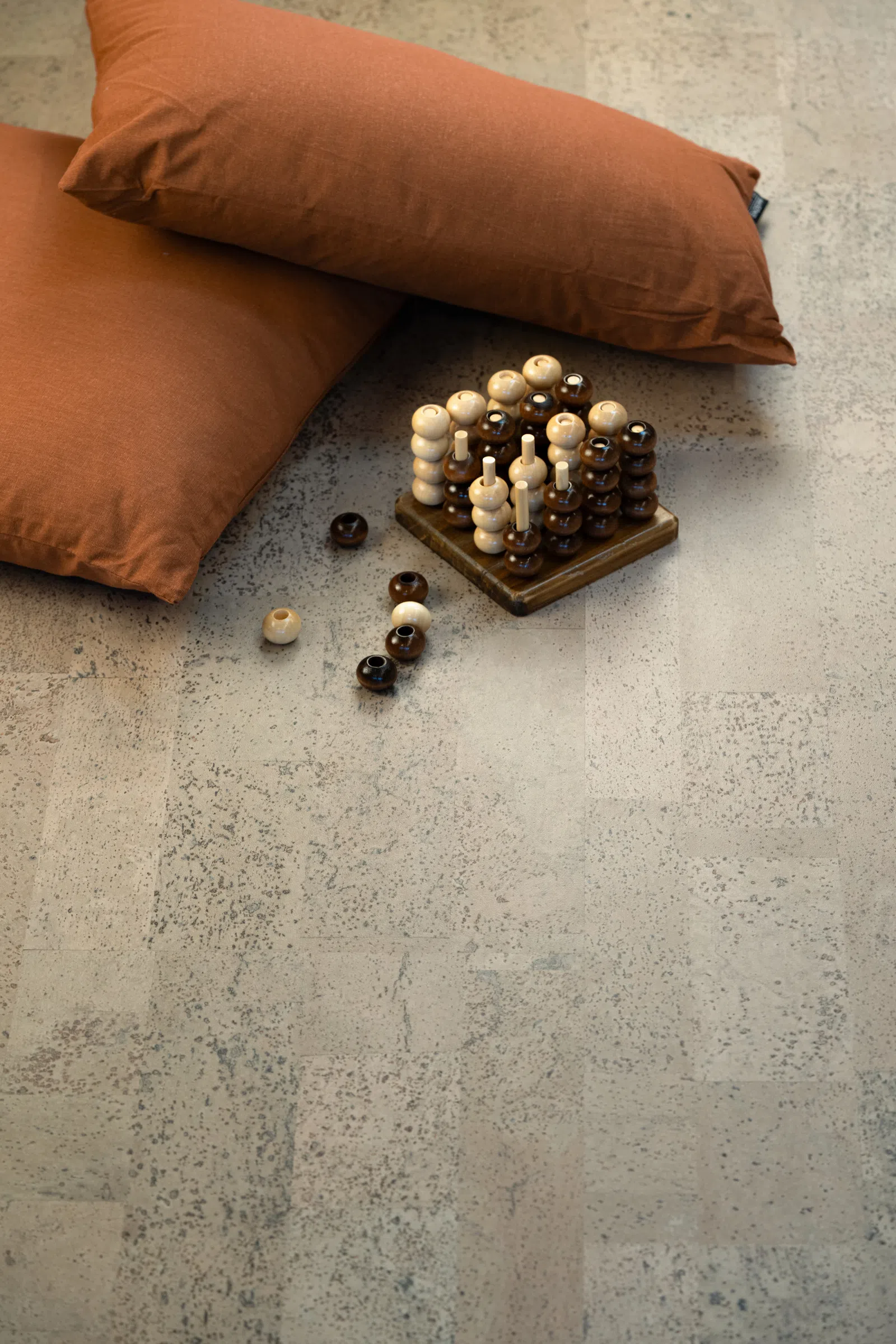 Wooden strategy game with light and dark pieces near two rust-colored cushions on a textured floor.