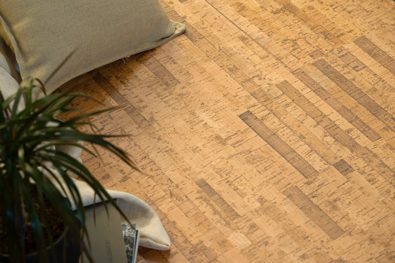 Close-up of natural cork flooring with a green plant and beige cushion on a light fabric in the corner.