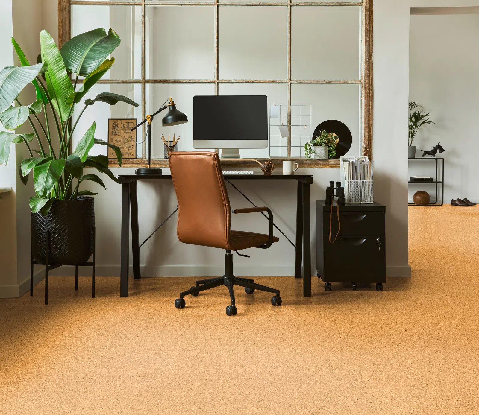 Modern home office setup with brown leather chair, computer, desk lamp, large plant, and wooden floor