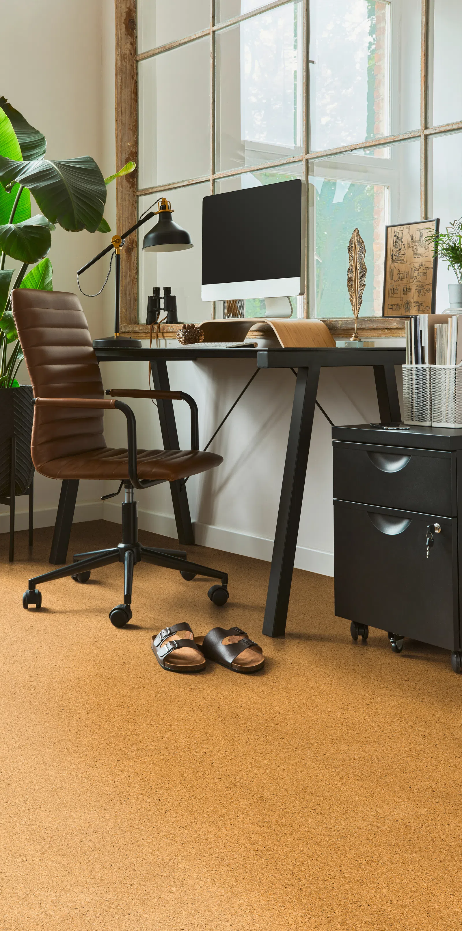 Modern home office setup with brown leather chair, black desk, computer, and large window with natural light