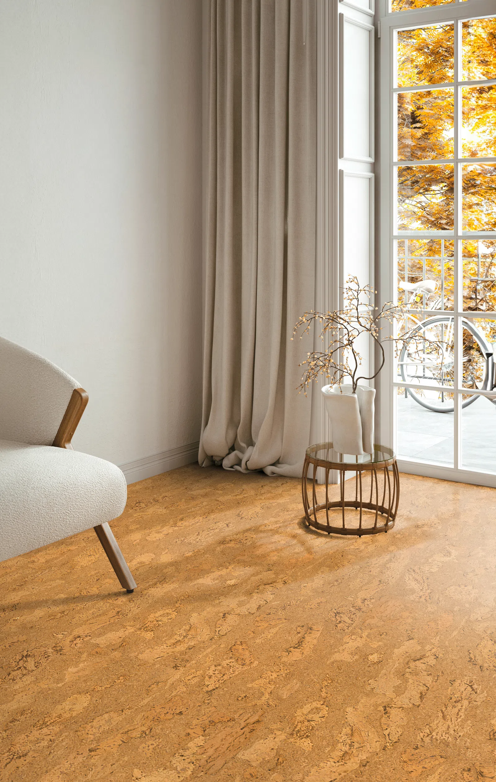 Cozy corner with beige armchair, long curtains, round table with vase, and sunlight from window showing autumn trees.